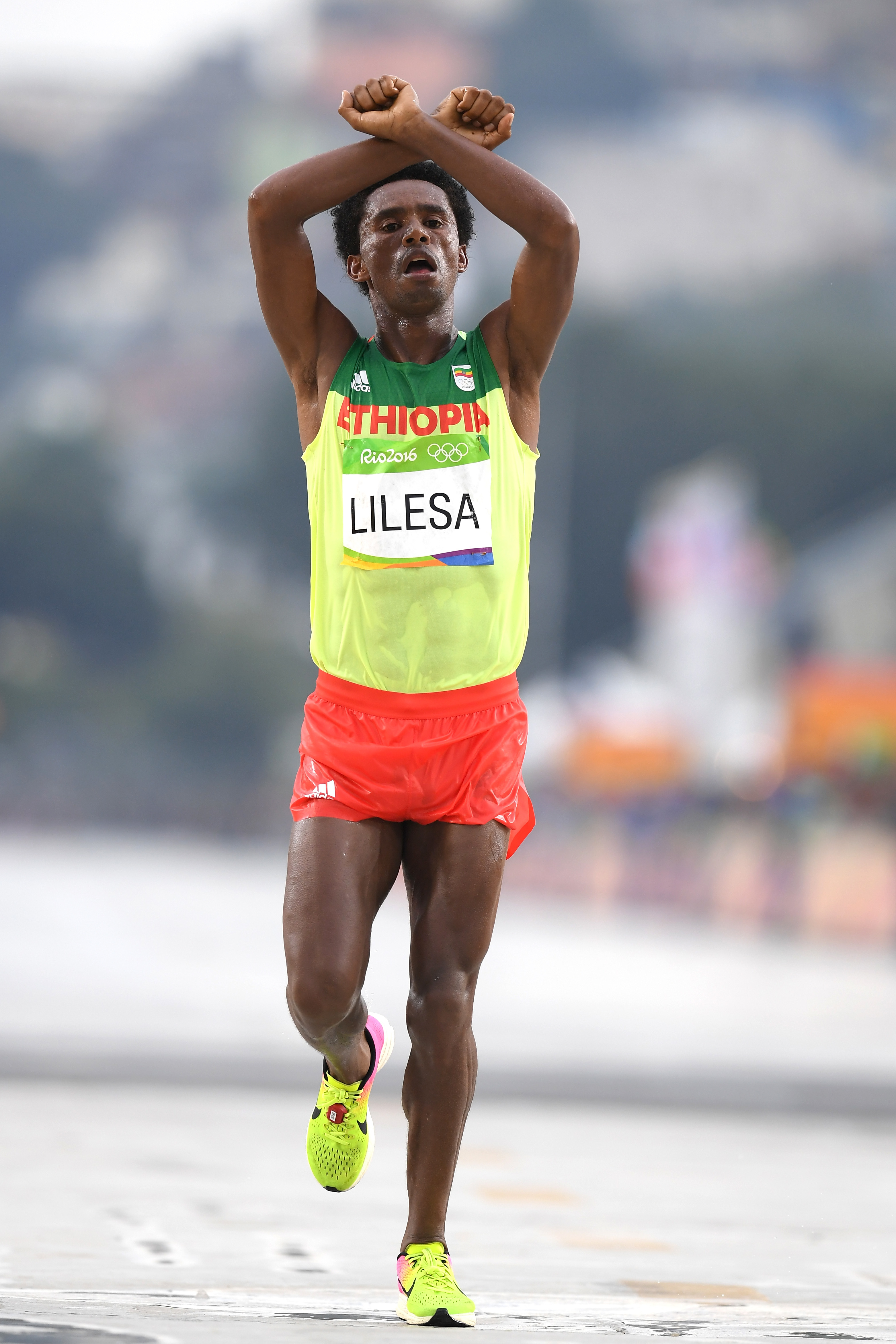 Feyisa Lilesa crosses the finish line with arms crossed over his head during a marathon, wearing athletic gear with "Ethiopia" and "Lilesa" printed on it