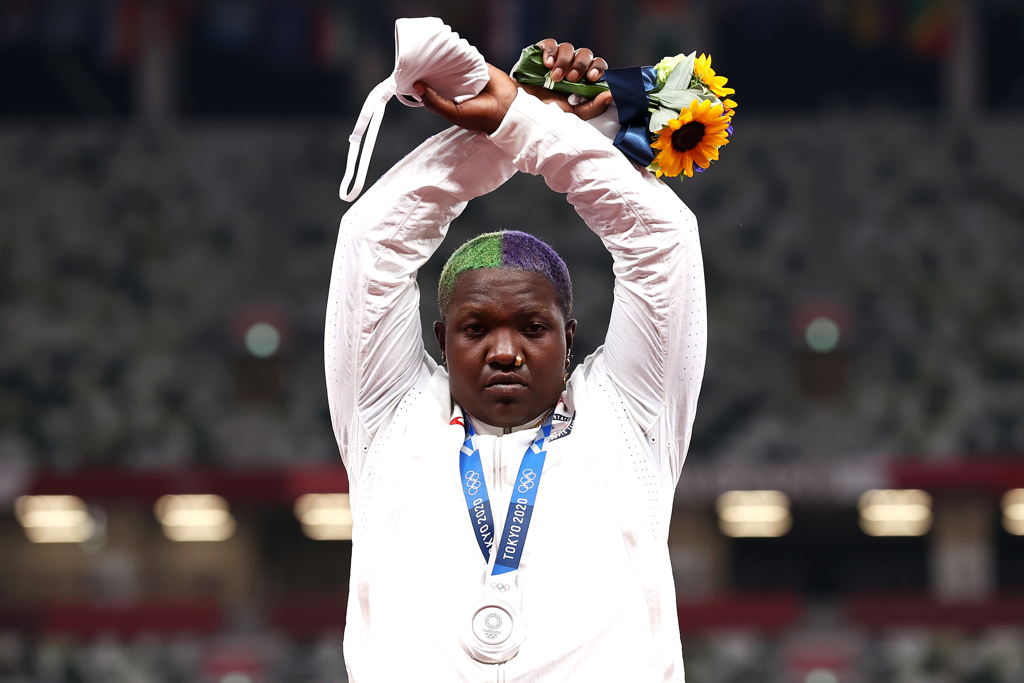 Raven Saunders at the Olympics, holding a bouquet and silver medal, arms crossed in an "X" above her head. They wears a white track jacket
