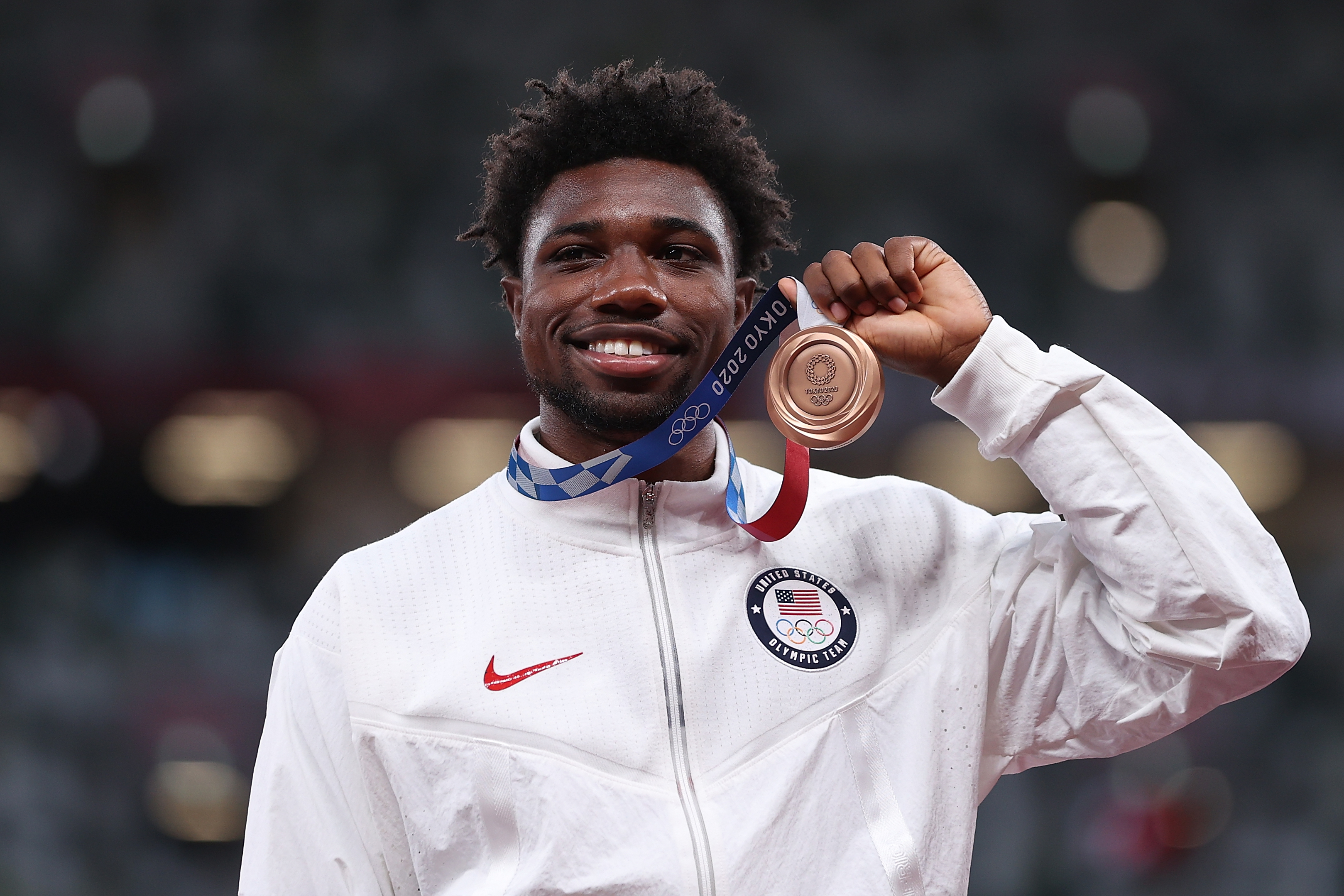 Male athlete in USA jacket smiling and holding up a bronze Olympic medal