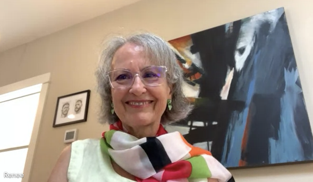 Renee is smiling in front of abstract art on the wall, wearing glasses and a multicolored scarf over a light top