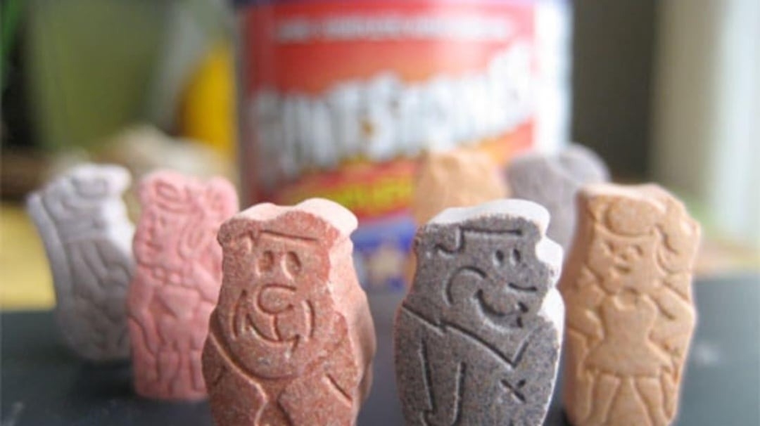 Fred and Wilma Flintstone Chewable Vitamins with a blurred vitamin bottle in the background