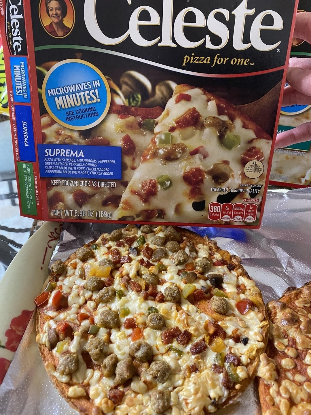 A hand holding a "Celeste pizza for one" box with an image of the Suprema flavor pizza on it. Below, a baked pizza on a tray shows its toppings