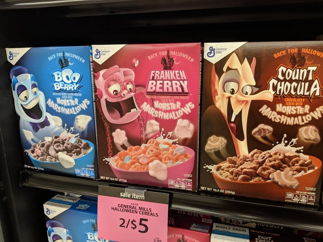 General Mills Halloween cereals on display: Boo Berry, Franken Berry, and Count Chocula. Sale sign reads "General Mills Halloween Cereals 2/$5."