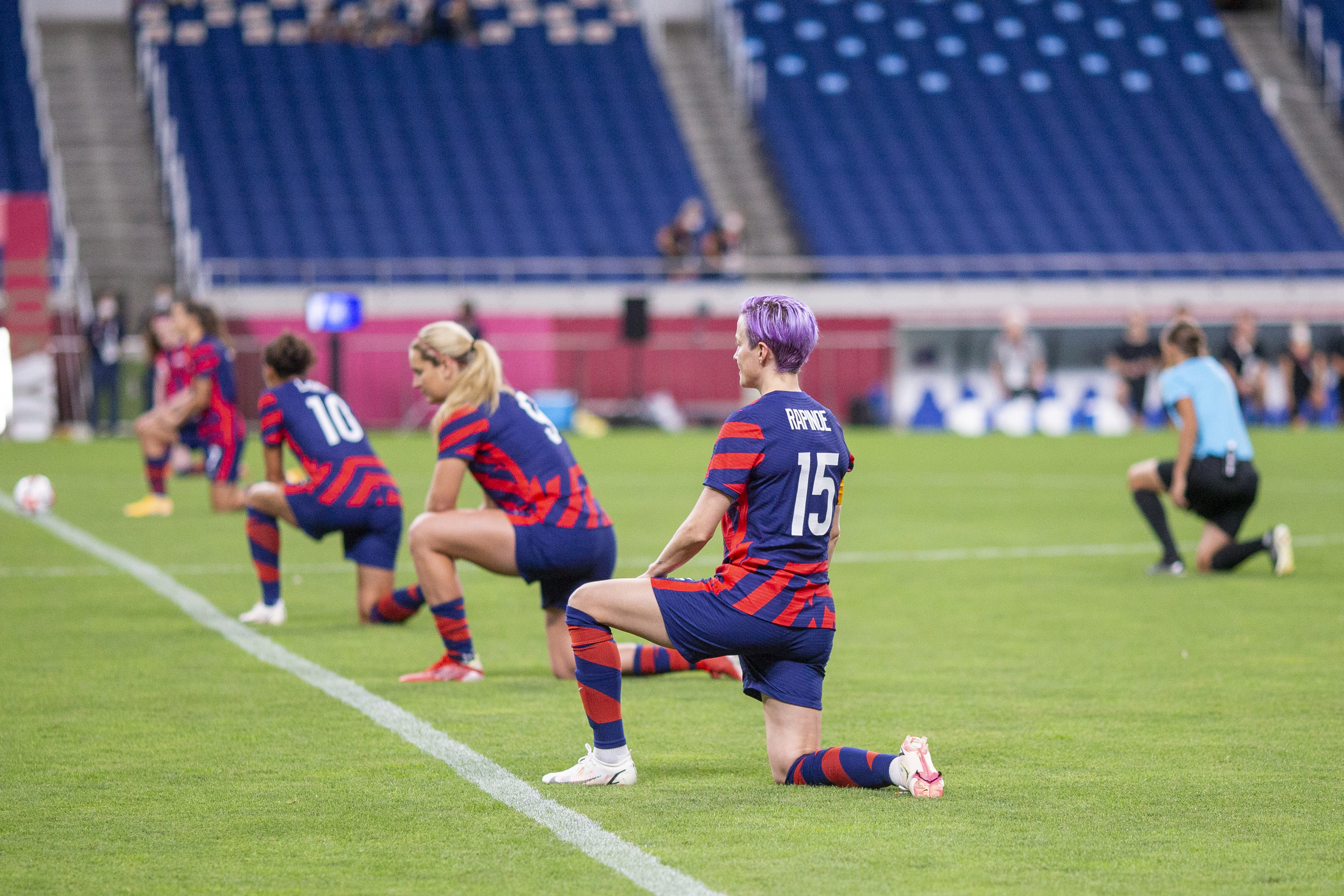 Megan Rapinoe and her teammates kneel on the soccer field during a game, wearing their team uniforms