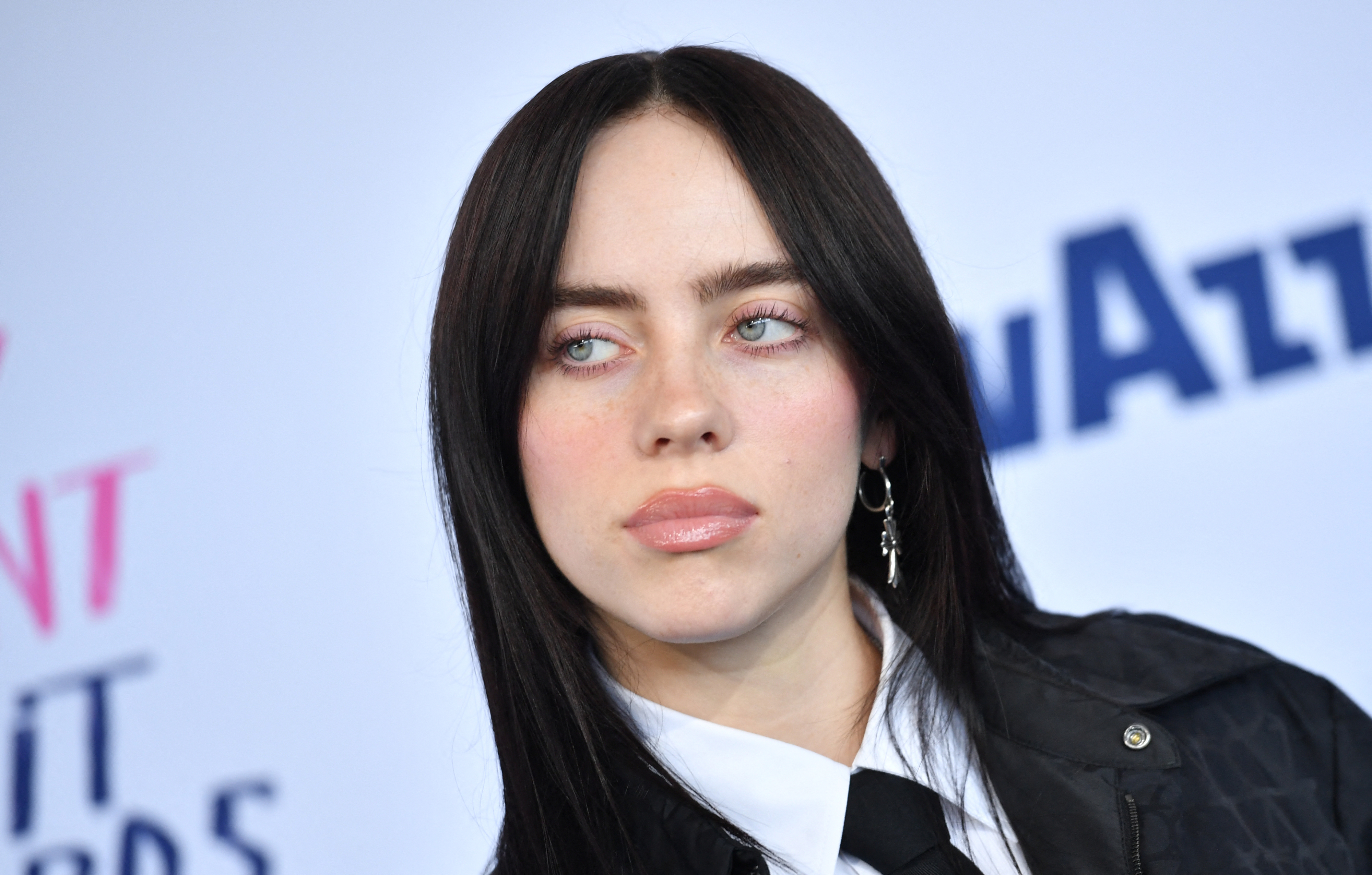 Billie Eilish at a red carpet event, wearing a black jacket and white shirt with a black tie