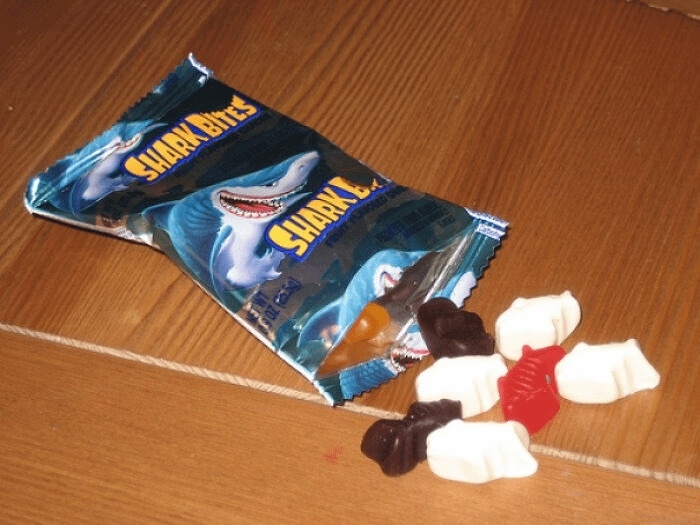 An open packet of Shark Bites fruit snacks with various gummy shark shapes spilling out onto a wooden surface
