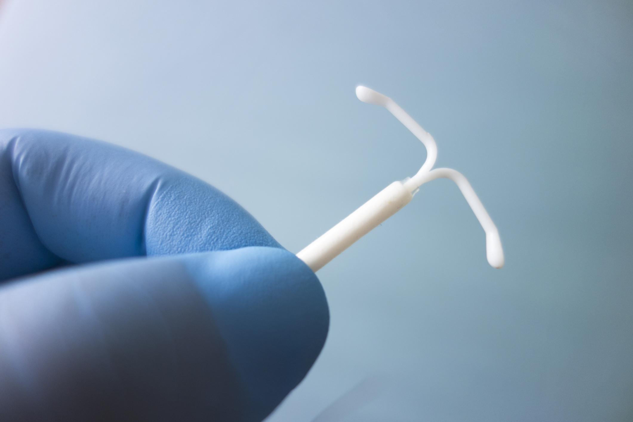 A gloved hand holds an intrauterine device (IUD) against a plain background