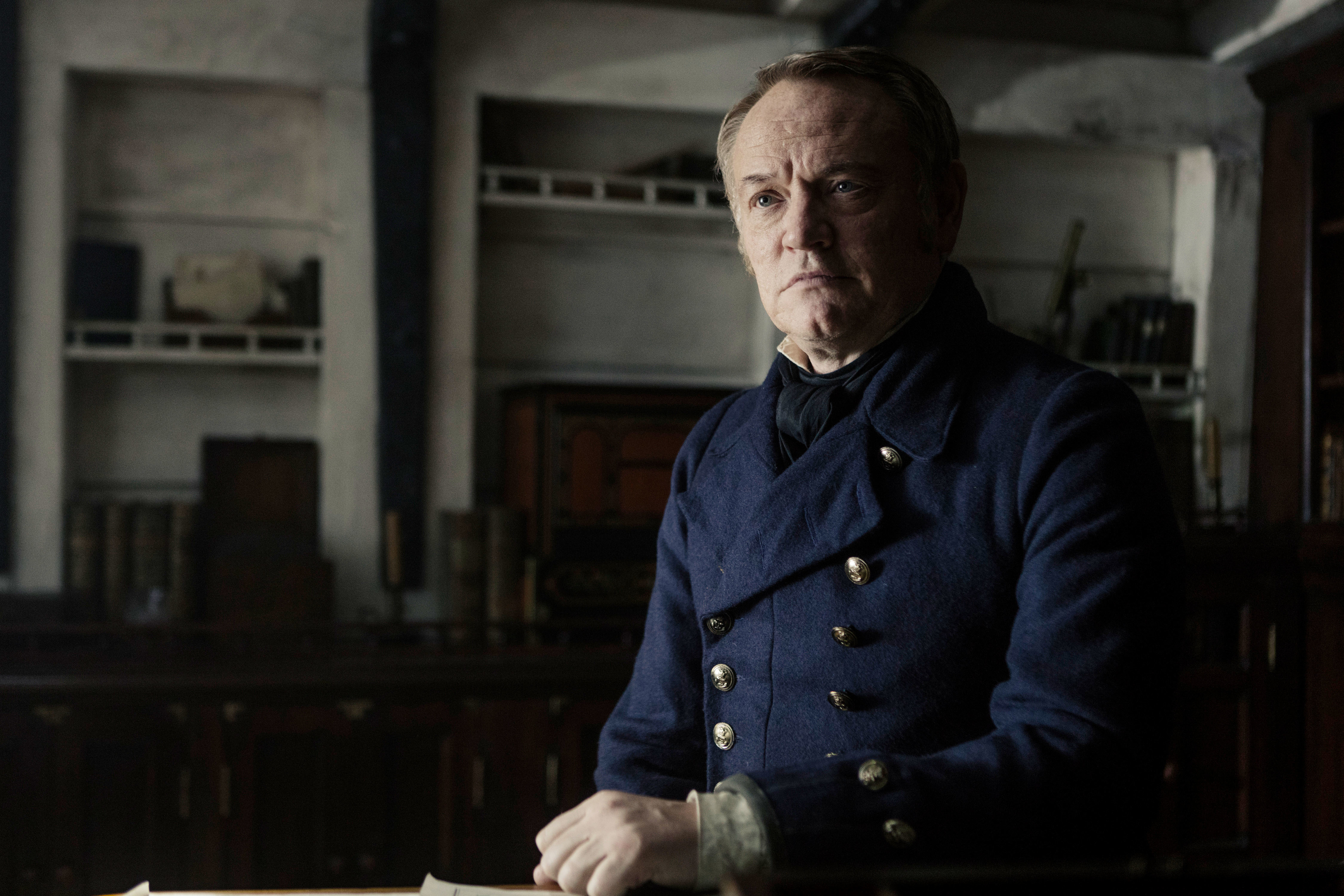 Jared Harris as Captain Francis Crozier in a period naval uniform, sitting in a dimly lit room with shelves and nautical items in the background