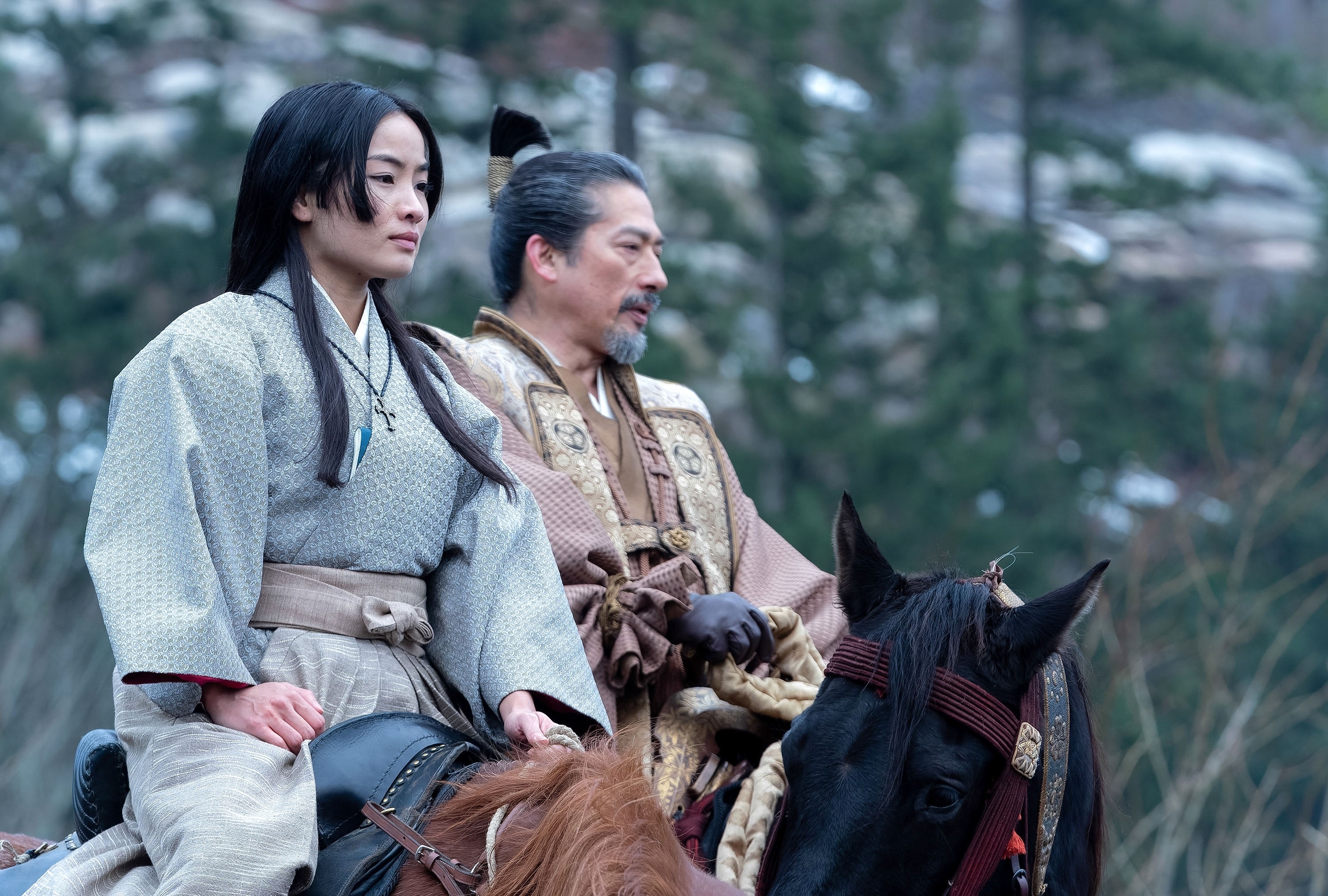 Anna Sawai and Hiroyuki Sanada in traditional period costumes ride horses in a forest setting in a scene