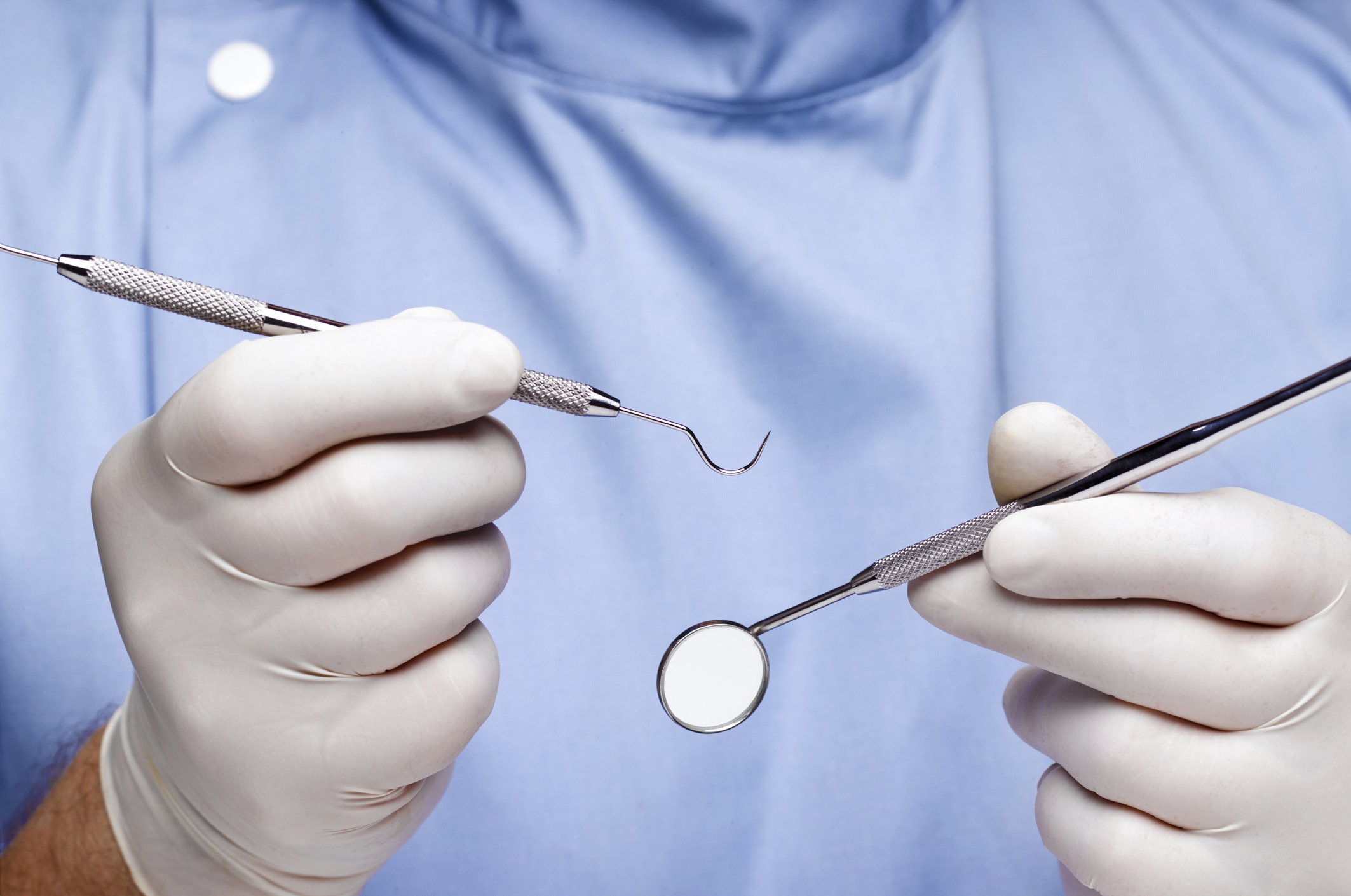 A dentist in gloves holding a dental probe and a dental mirror, preparing for an examination