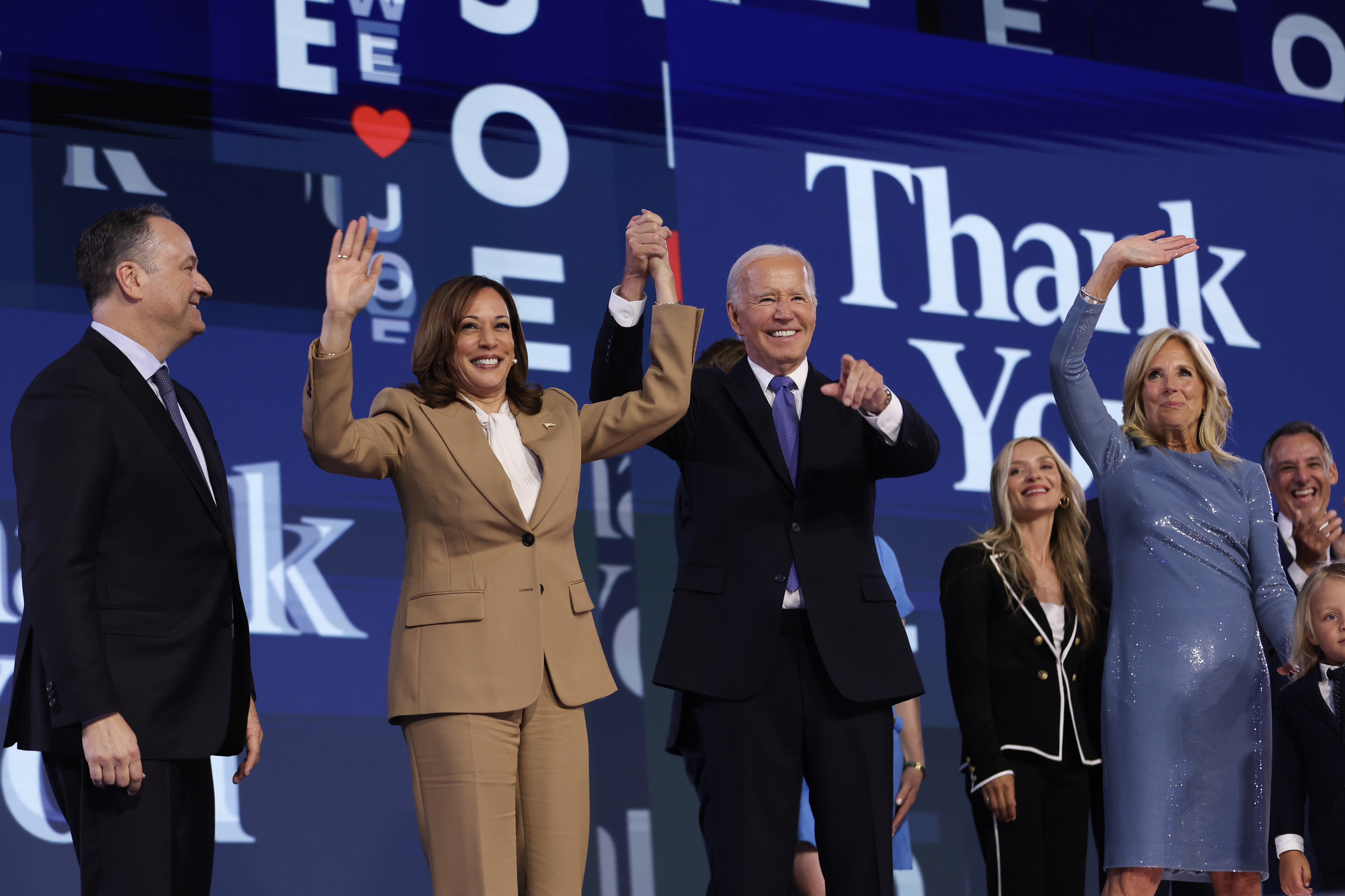 Kamala Harris, Joe Biden, Jill Biden, and Doug Emhoff stand on stage smiling and waving, dressed in formal attire, with &quot;Thank You&quot; written in the background