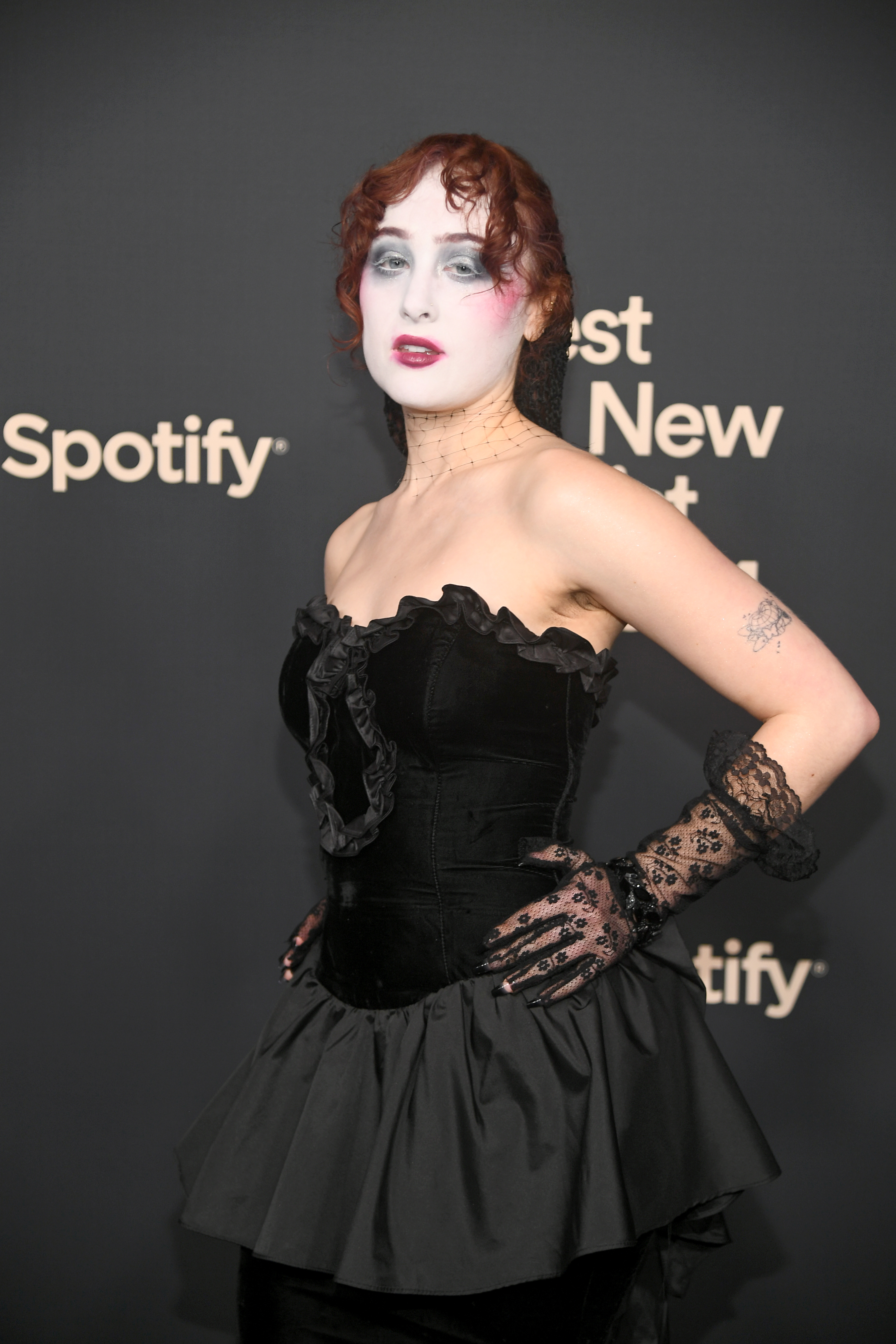 Zheani on a red carpet wearing a black strapless dress with lace gloves