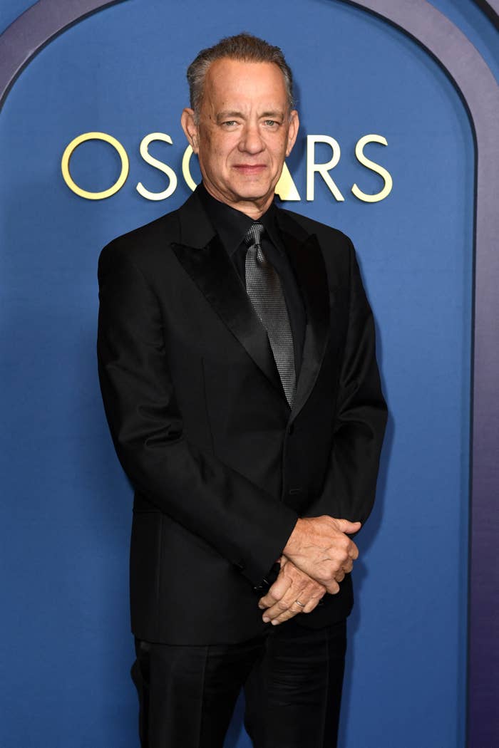 Tom Hanks stands in a classic suit with a dark tie at an Oscars event