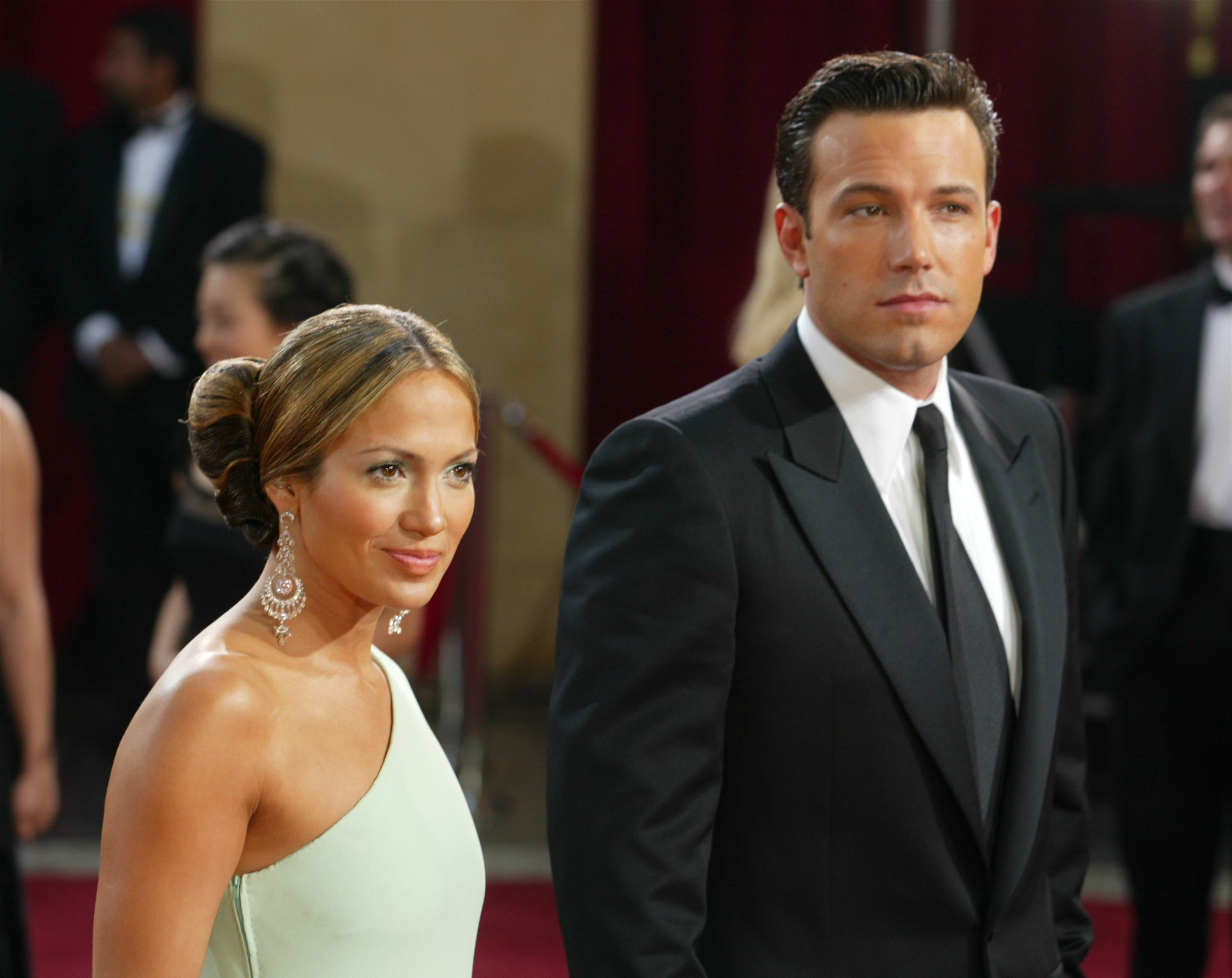 Jennifer Lopez and Ben Affleck on the red carpet; Jennifer in an elegant sleeveless gown and statement earrings, Ben in a classic black suit and tie