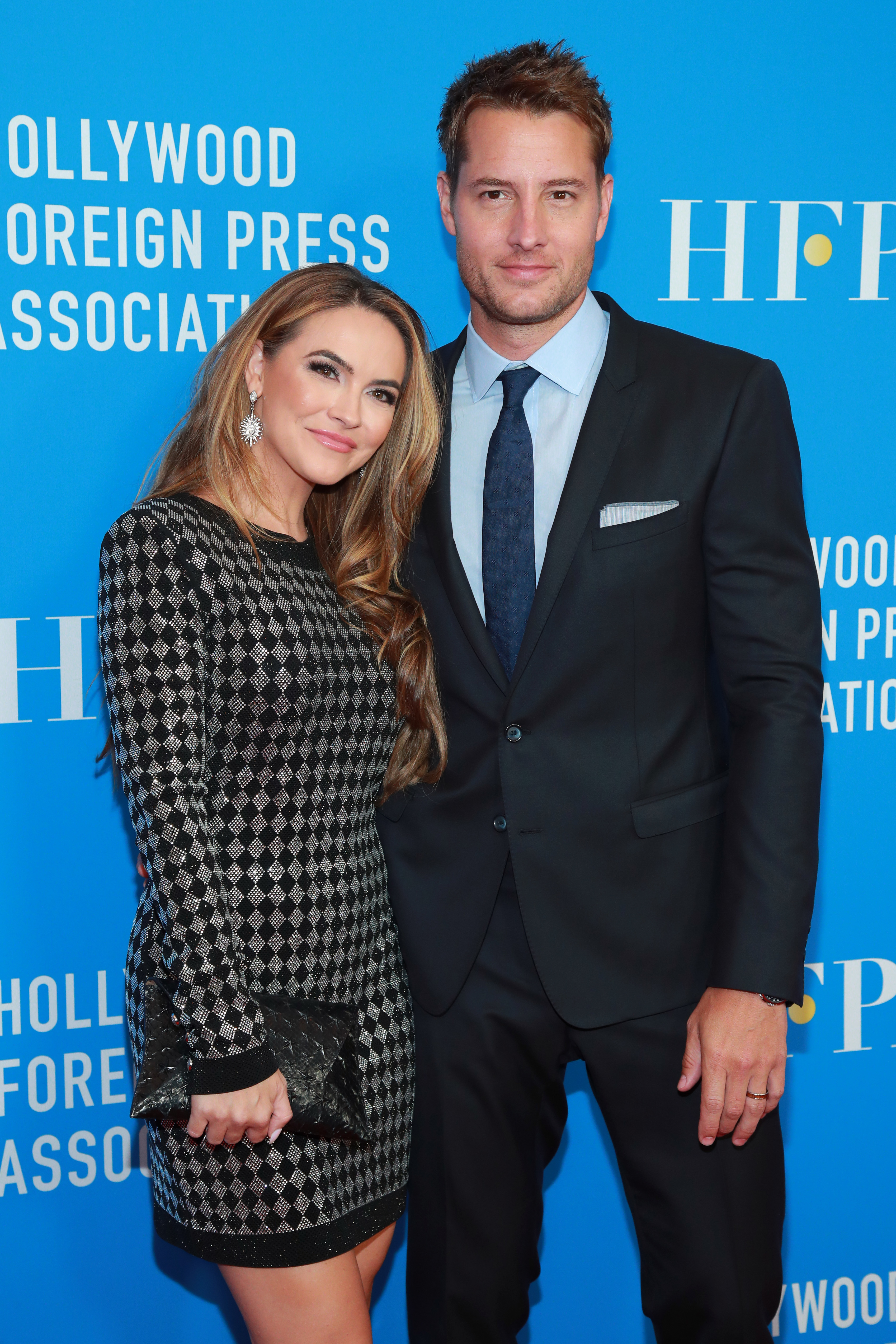 Chrishell Stause and Justin Hartley pose together at a Hollywood Foreign Press Association event; Chrishell wears a patterned dress, and Justin wears a suit and tie
