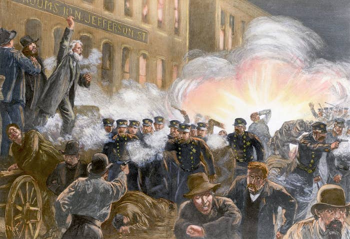 Illustration of the Haymarket Riot with police clashing with protesters, an explosion occurring in the background, and chaos ensuing in the street