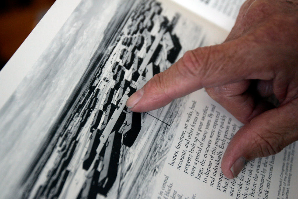 A close-up of a hand pointing to a black and white photograph of a historical site along with accompanying text in a book