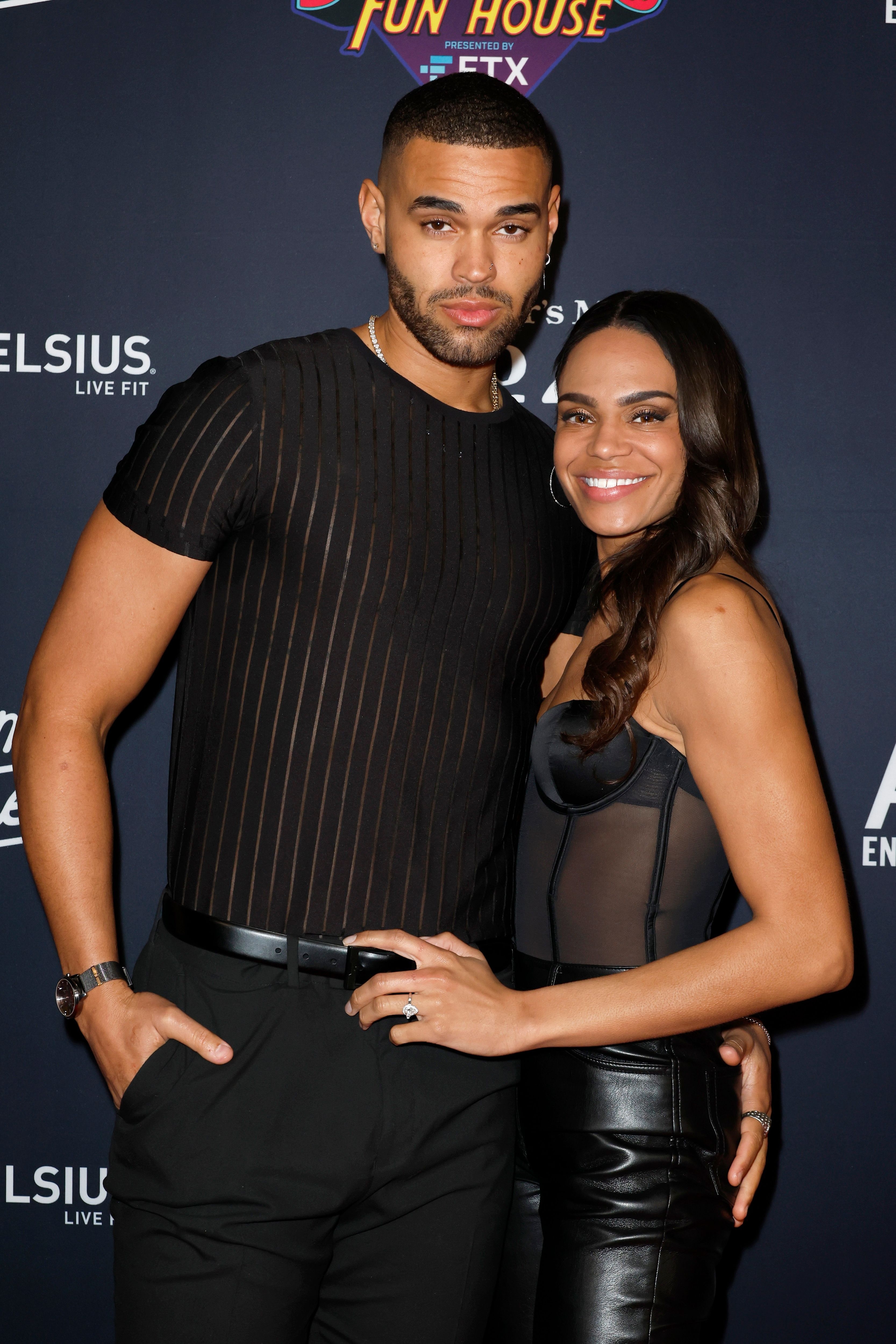 Nayte Olukoya in a striped shirt and Michelle Young in a strapless top and leather pants, posing together at an event