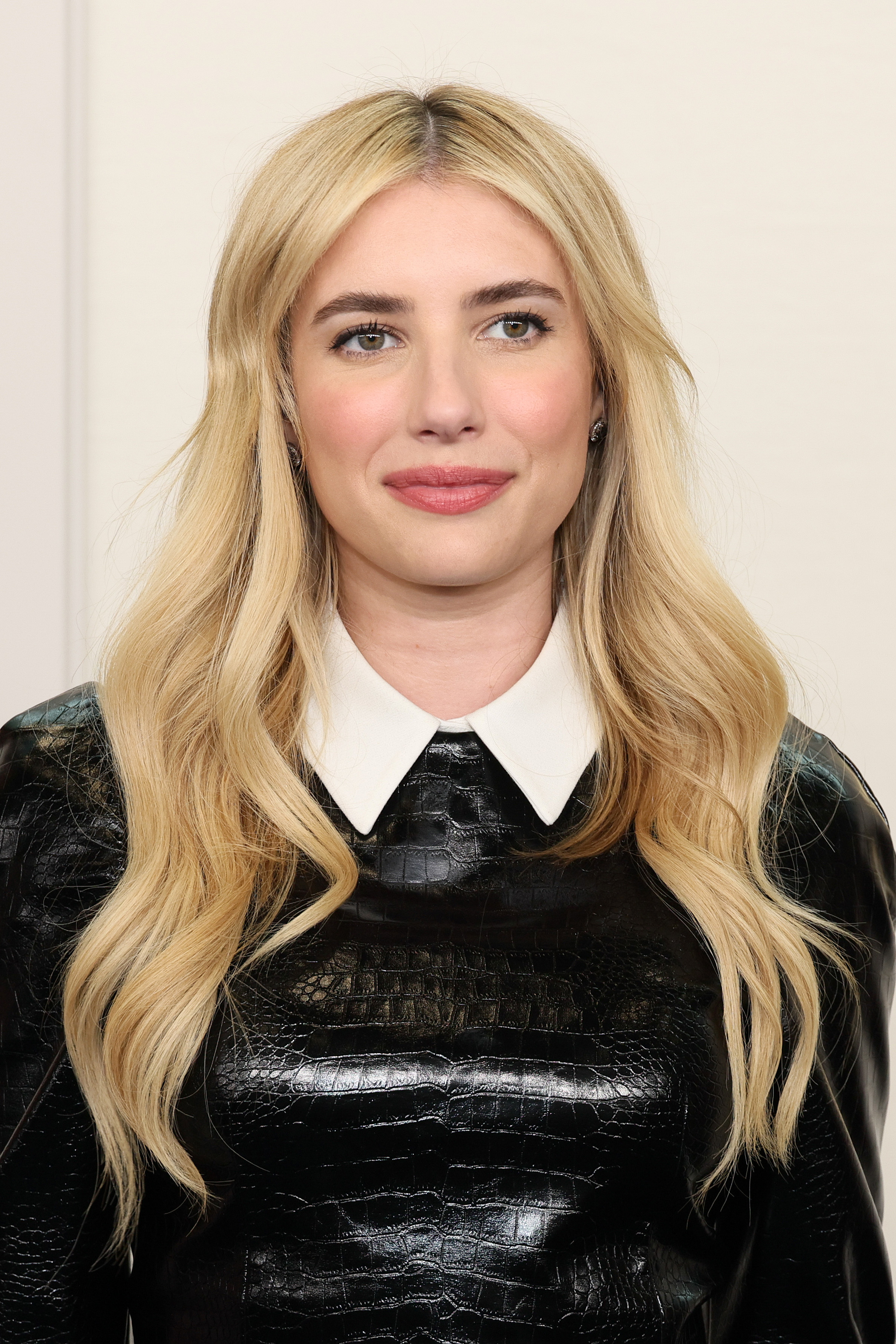 Emma Roberts wearing a shiny dress with a collar, smiles at the camera