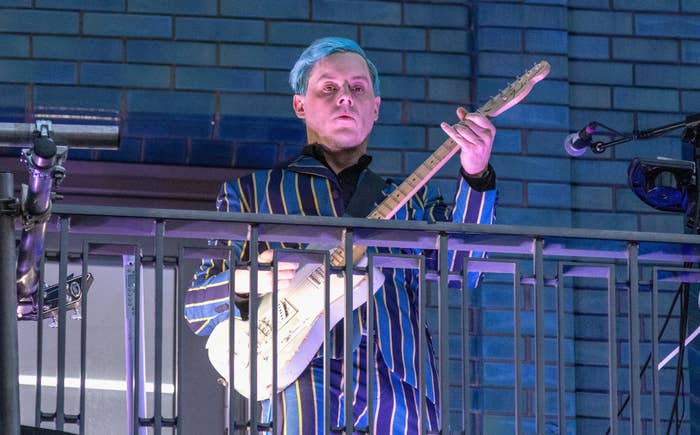 Jack White plays an electric guitar on a balcony, wearing a striped suit