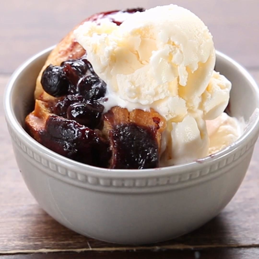 Bowl of a warm dessert topped with blueberries and a scoop of vanilla ice cream