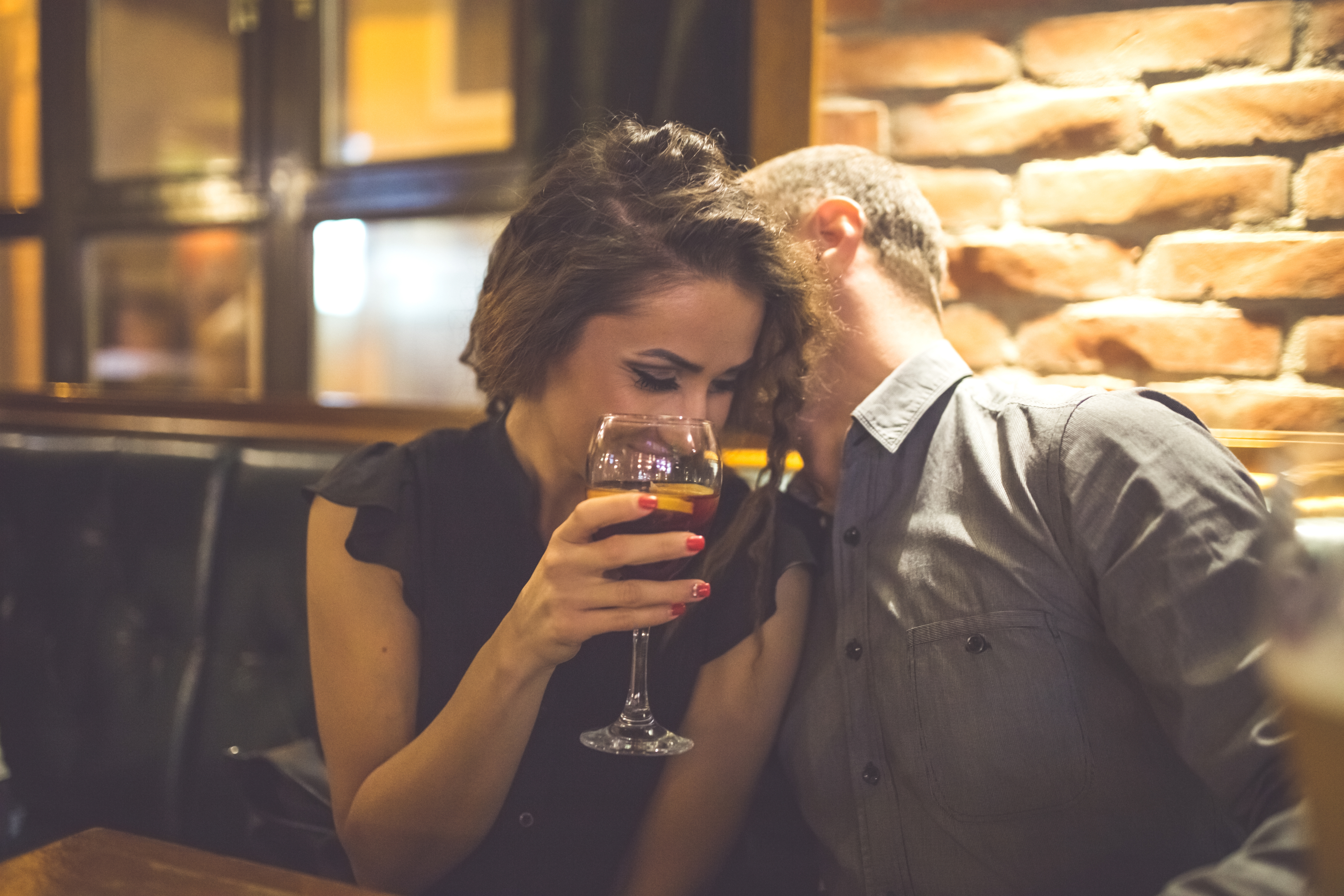 A woman and a man share a moment at a cozy bar. The woman smiles while holding a wine glass