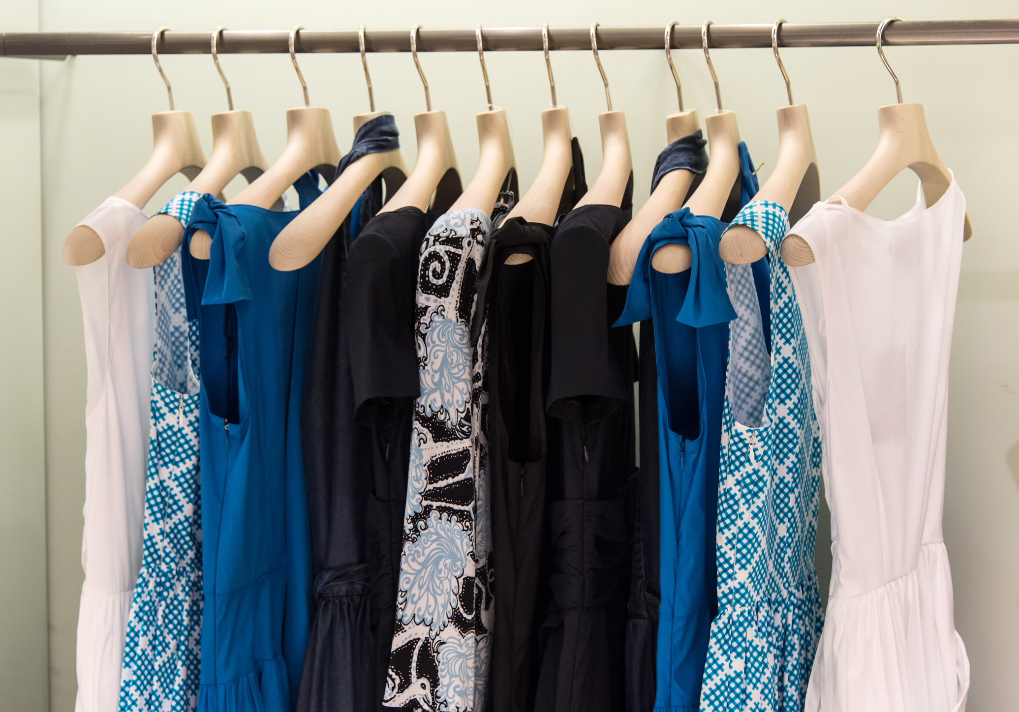 Various blue, black, and white patterned dresses on hangers in a clothing store display