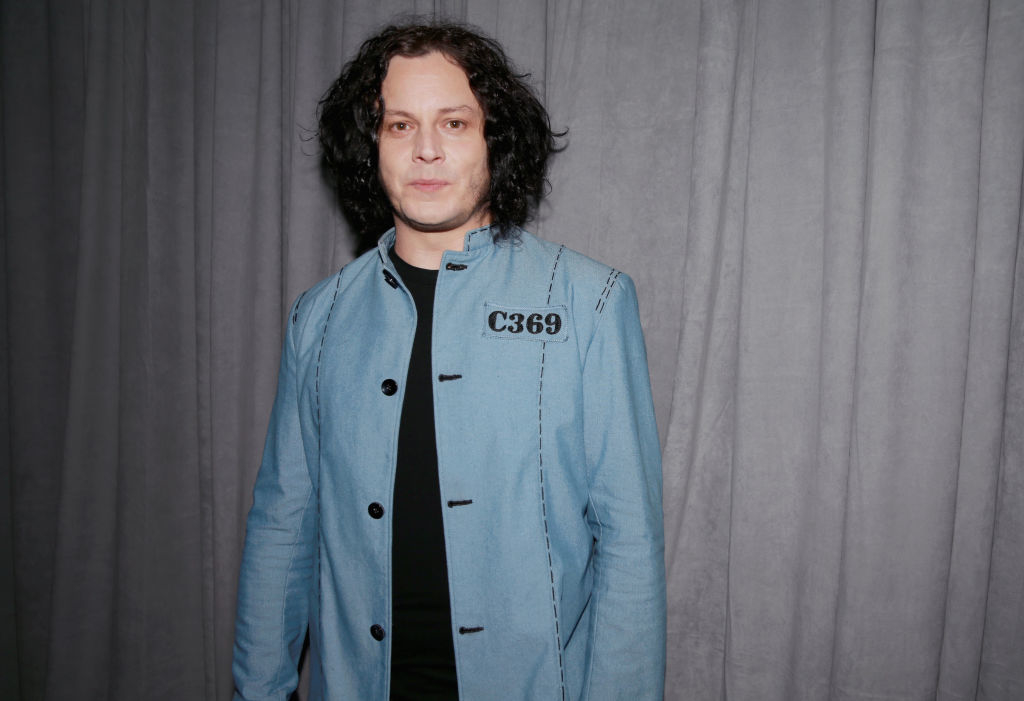 Jack White wearing a light-colored jacket with a shirt, standing in front of a plain backdrop