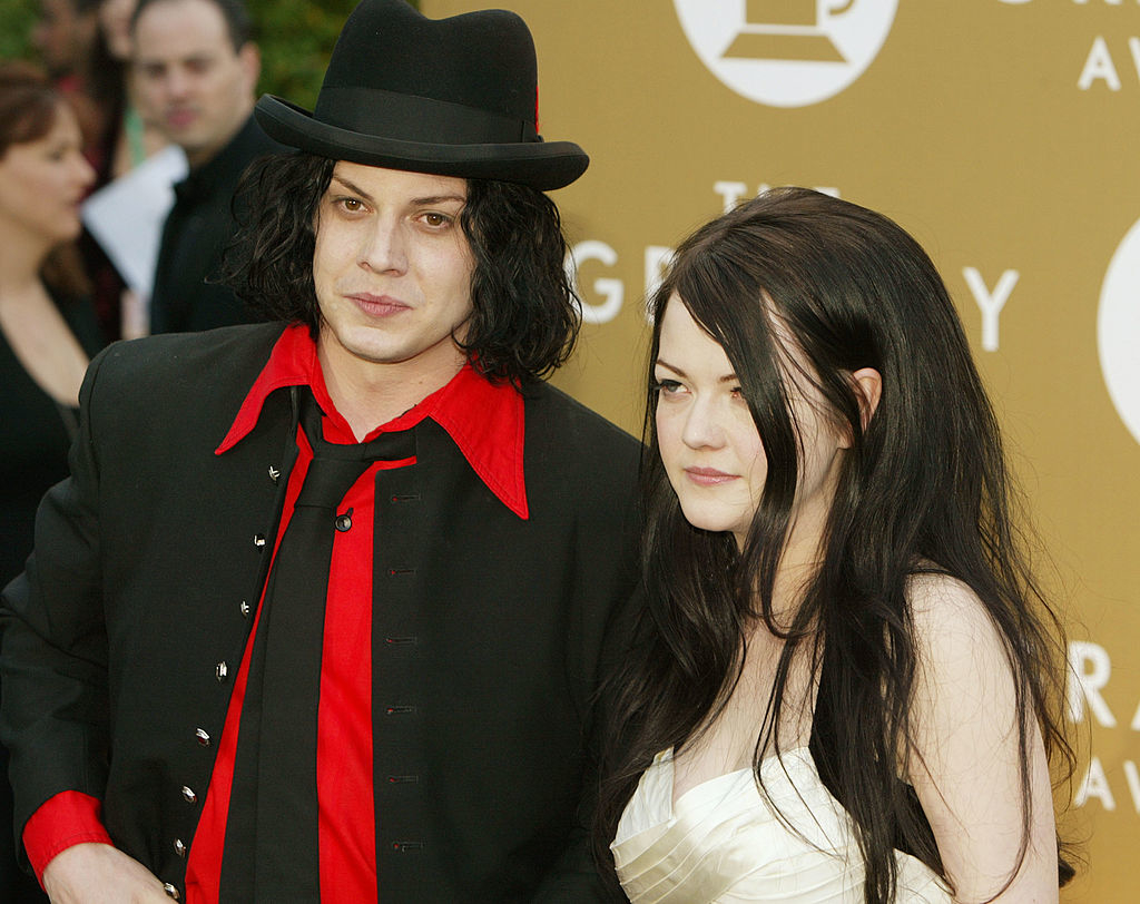 Jack White and Meg White on the red carpet at the Grammy Awards. Jack wears a dark suit with a shirt and tie, and Meg wears a strapless dress