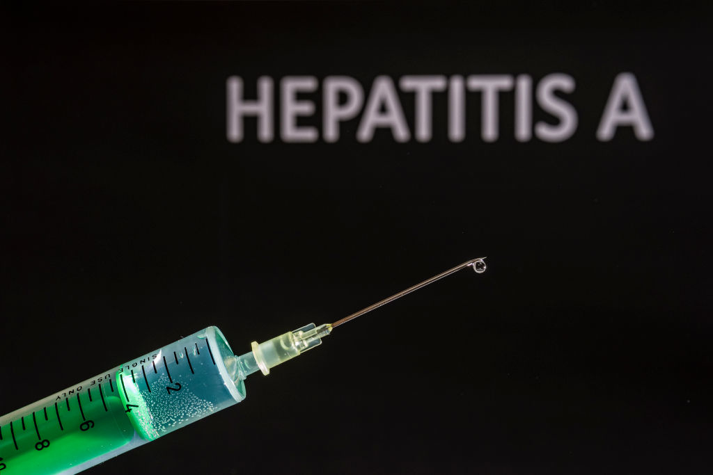 A syringe with a drop at the tip is shown in front of the word &quot;Hepatitis A&quot; on a black background