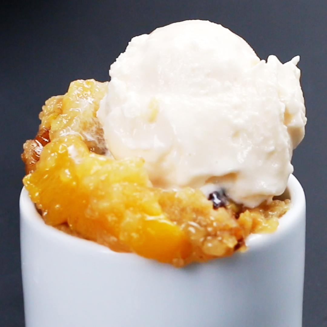 Peach cobbler topped with vanilla ice cream in a white ramekin