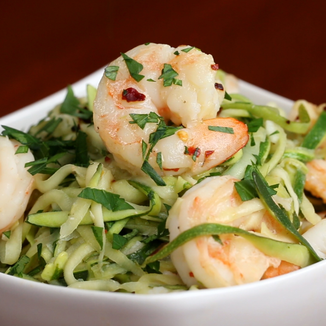 A close-up of a dish featuring shrimp served on a bed of zucchini noodles, garnished with chopped herbs