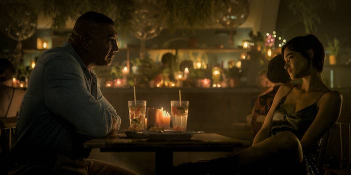 Dave Bautista and Sofia Boutella sit across from each other at a dimly lit table in a restaurant with candles and soft lighting