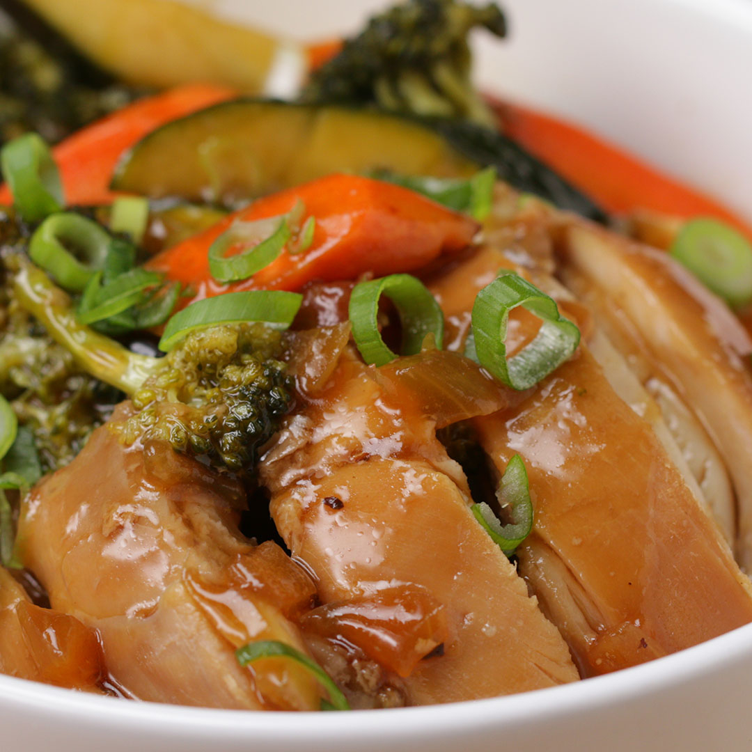 Closeup of a dish with glazed chicken, mixed vegetables, and sliced green onions in a white bowl