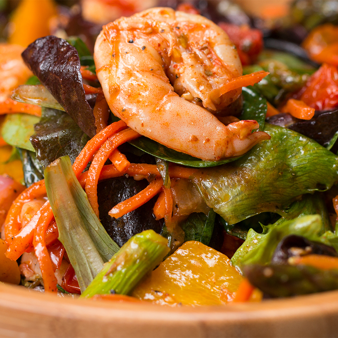 Close-up of a shrimp salad with mixed greens, carrots, bell peppers, and various vegetables. The salad appears fresh and well-seasoned