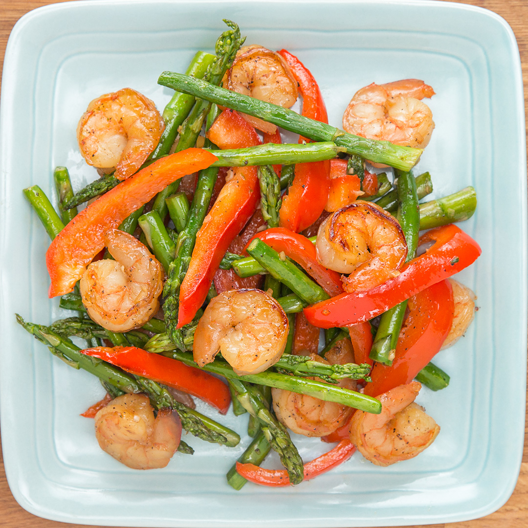 A plate with shrimp, asparagus, and red bell peppers, arranged neatly