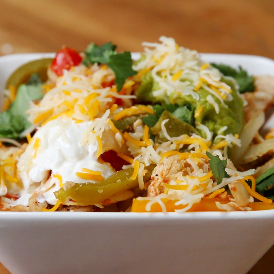 A bowl of loaded chicken nachos topped with shredded cheese, sour cream, guacamole, and fresh cilantro
