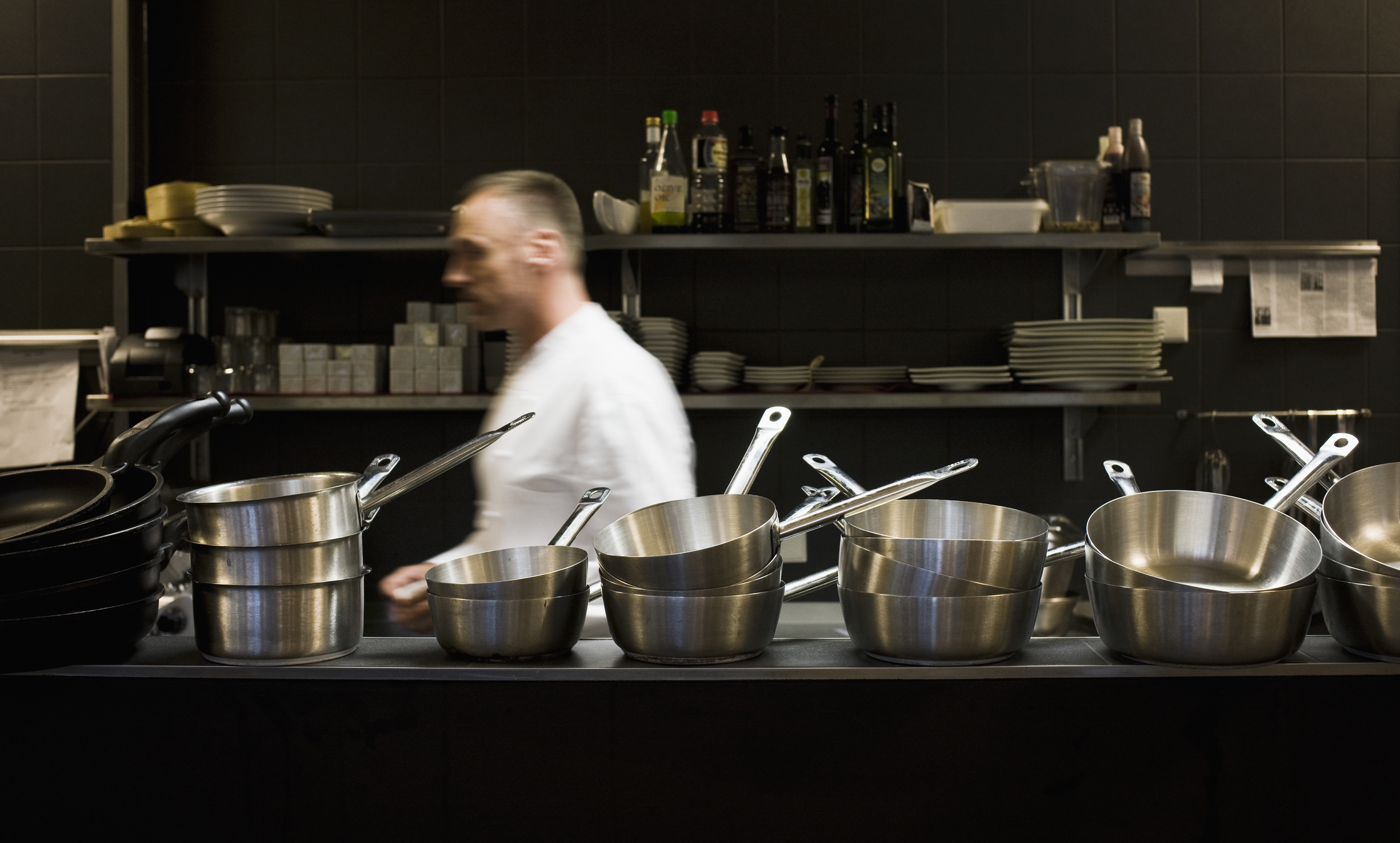 Chef in a professional kitchen with a row of stainless steel pots and pans in the foreground