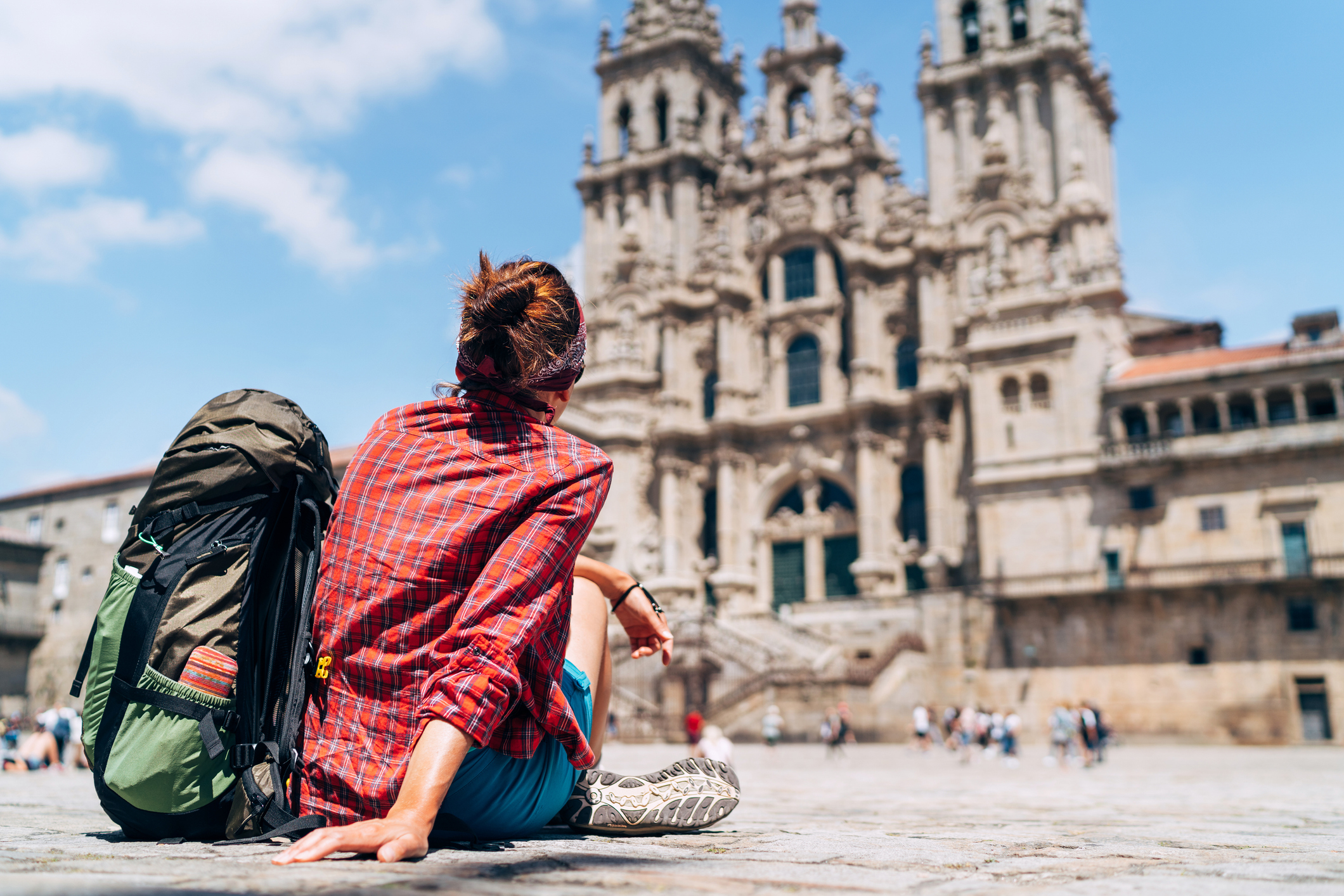 A traveler with a large backpack sits in front of a historic cathedral, admiring the architecture