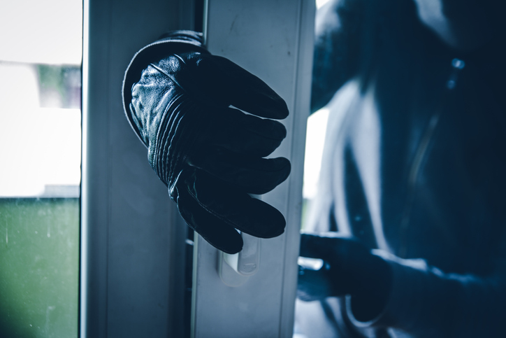 A gloved hand opening a glass door, depicting a potential burglary or break-in scenario