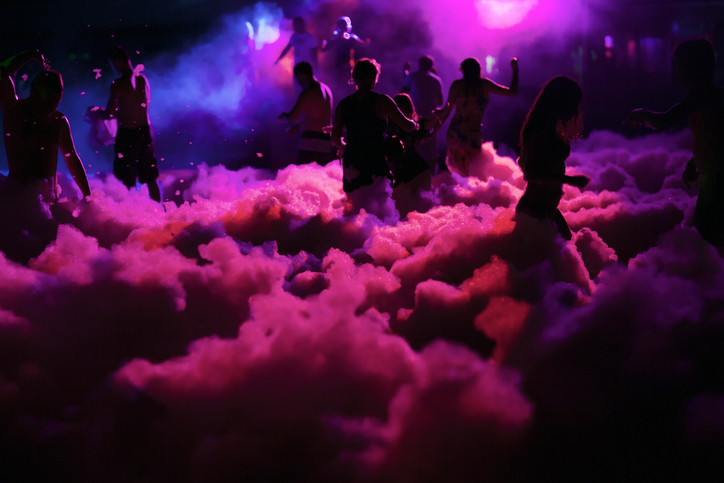 People dance amidst foam and lights at an outdoor event
