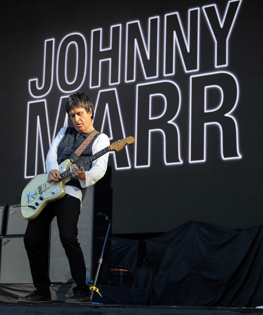 Johnny Marr plays guitar on stage in front of a large screen