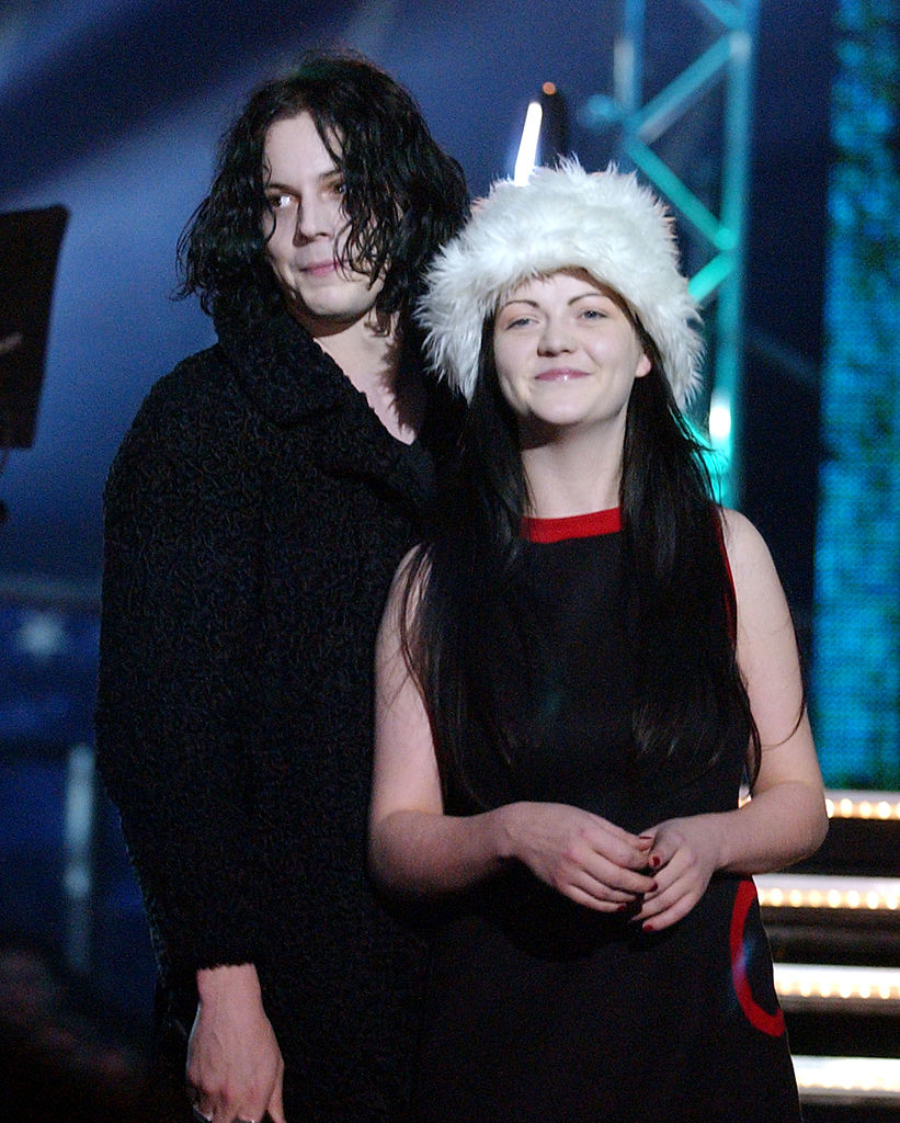 Jack White and Meg White pose together; Jack wears a dark textured coat, and Meg wears a dress with a fluffy hat
