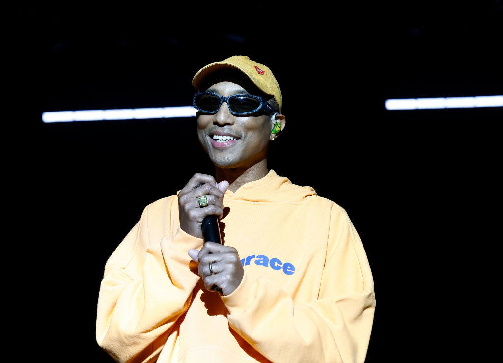 Pharrell Williams smiles while holding a microphone