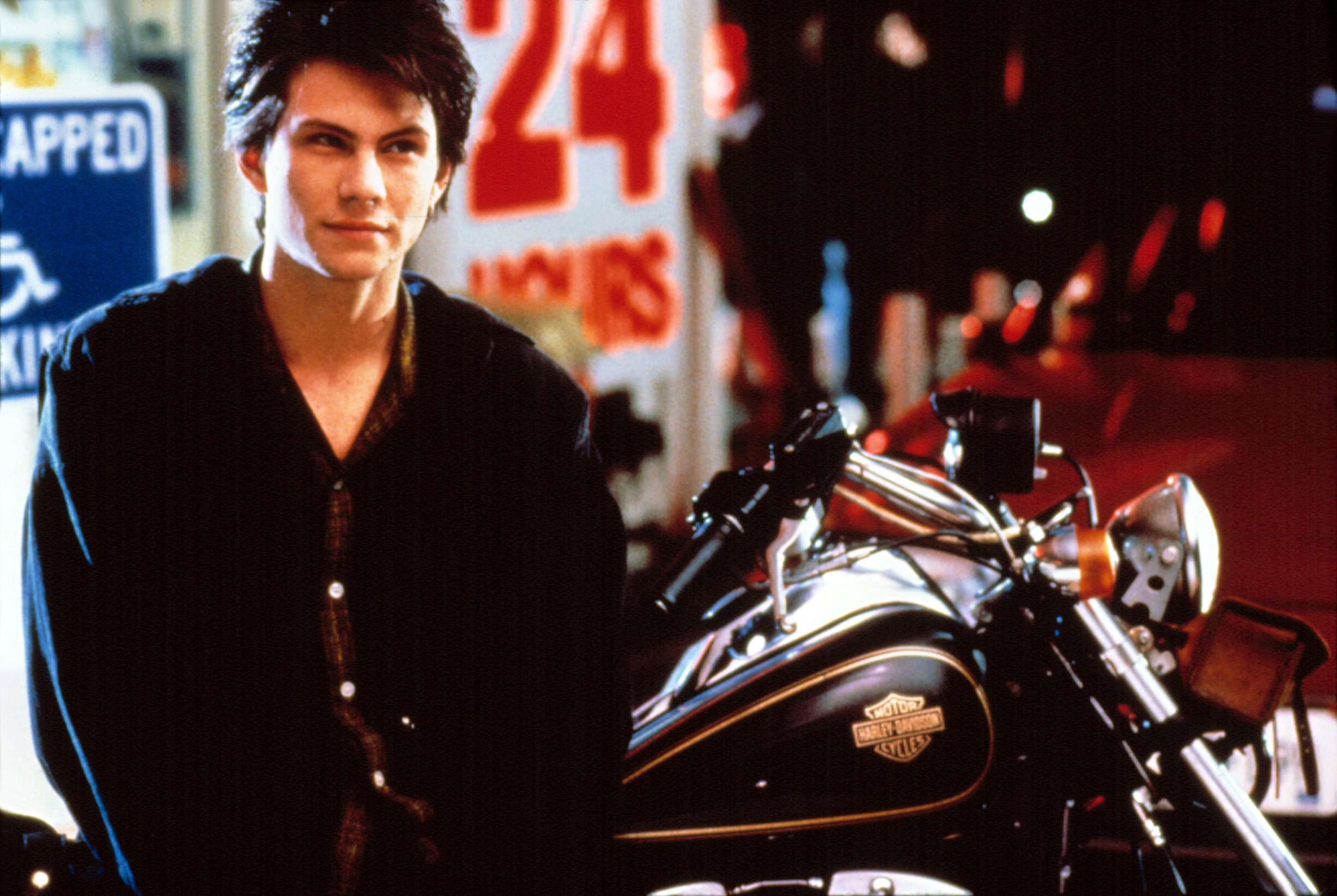 Christian Slater leaning against a Harley-Davidson motorcycle in "Heathers"