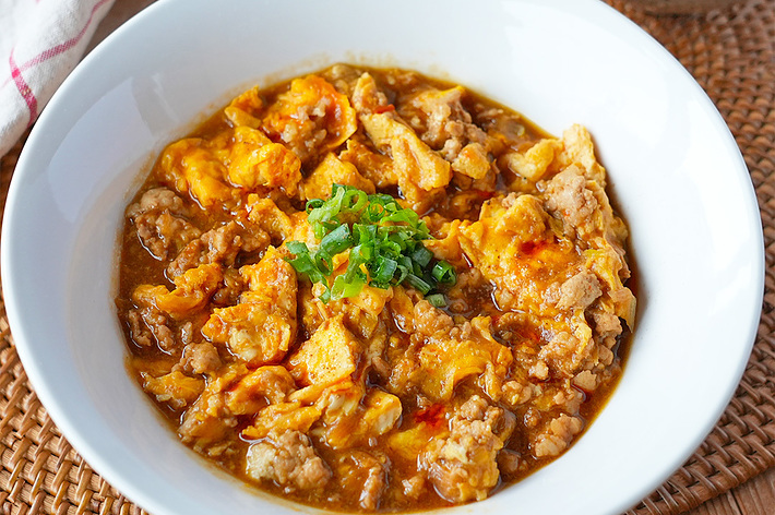 おいしそうな麻婆豆腐が盛られた白い皿と、米が入った小さなボウルがテーブルに置かれています。