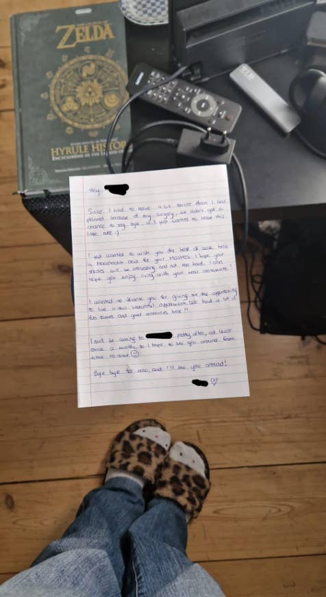 A handwritten letter on the floor near leopard print slippers, a Nintendo Switch, and a Legend of Zelda book. The letter contains a personal note but is not readable