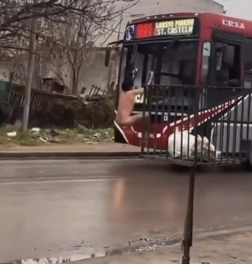 A bus with a sign reading "SARRIO MARIN ST. CASTEL" stands near a bus stop on a rainy day. No people are visible nearby