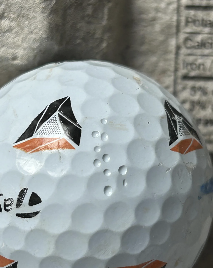 A close-up of a golf ball with several black and orange triangular designs and small engraved dots on its surface