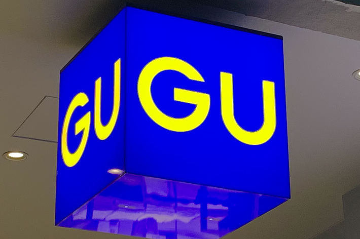 Bright store sign with &ldquo;GU&rdquo; in large yellow letters on a blue background hanging from the ceiling